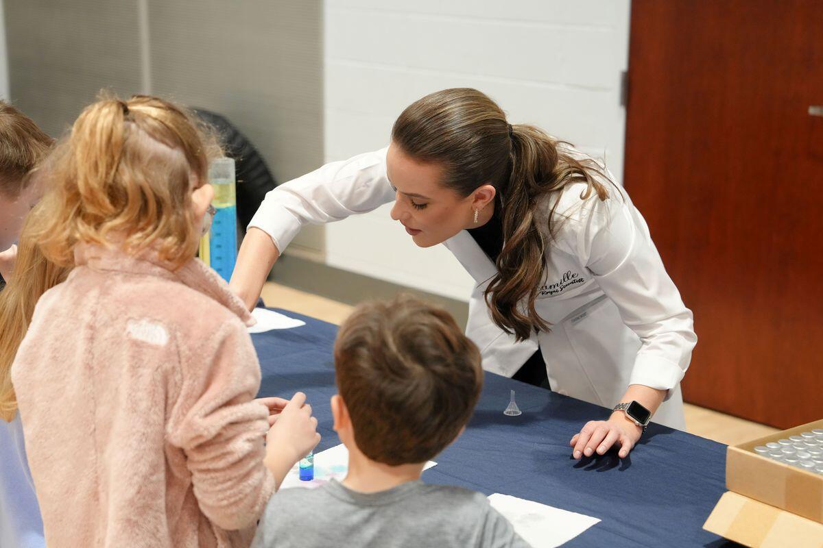 A photo of a woman demonstrating something on a table in front of two children. 