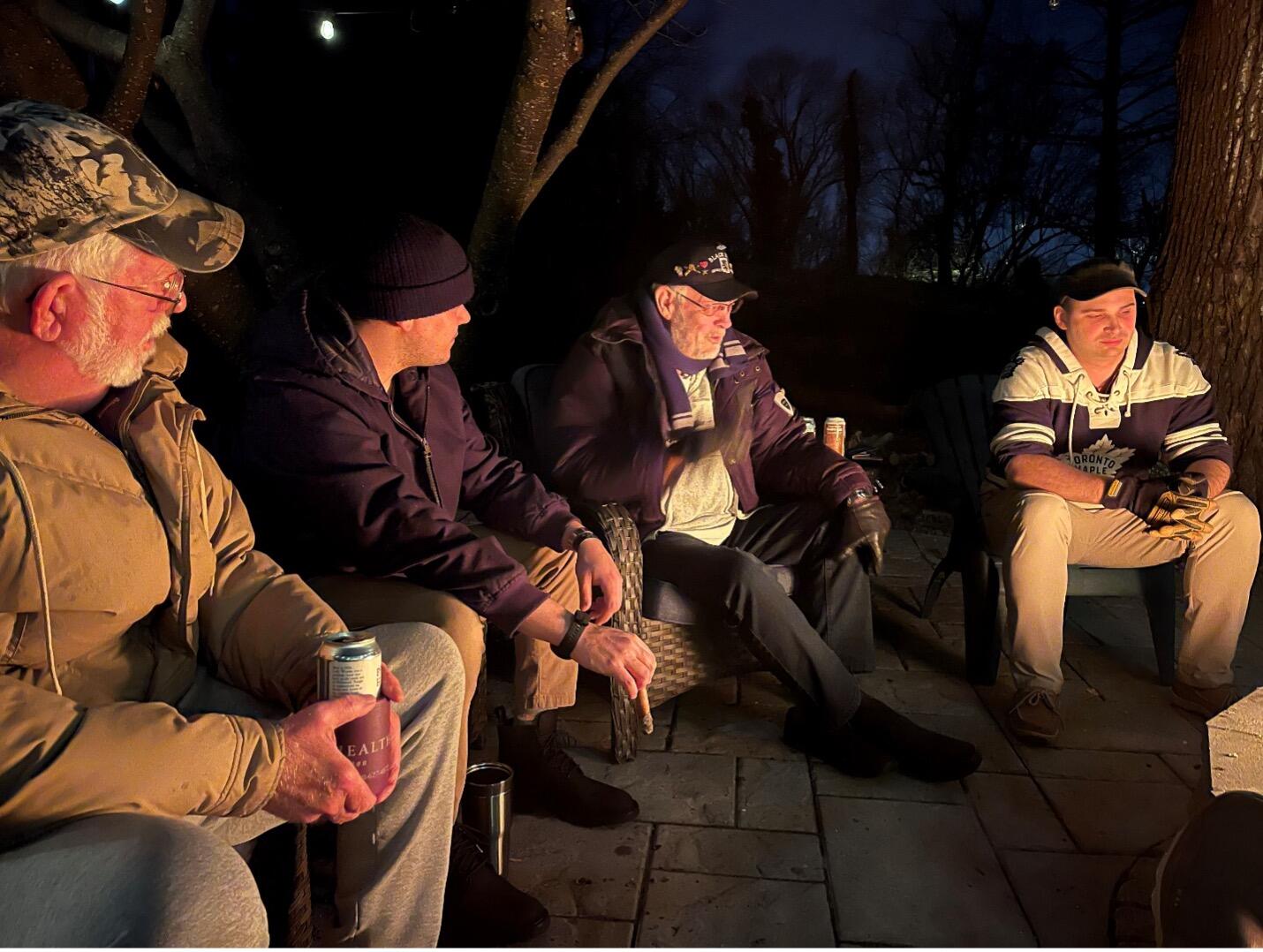 A photo of four men sitting outside in the dark in a semi-circle. 