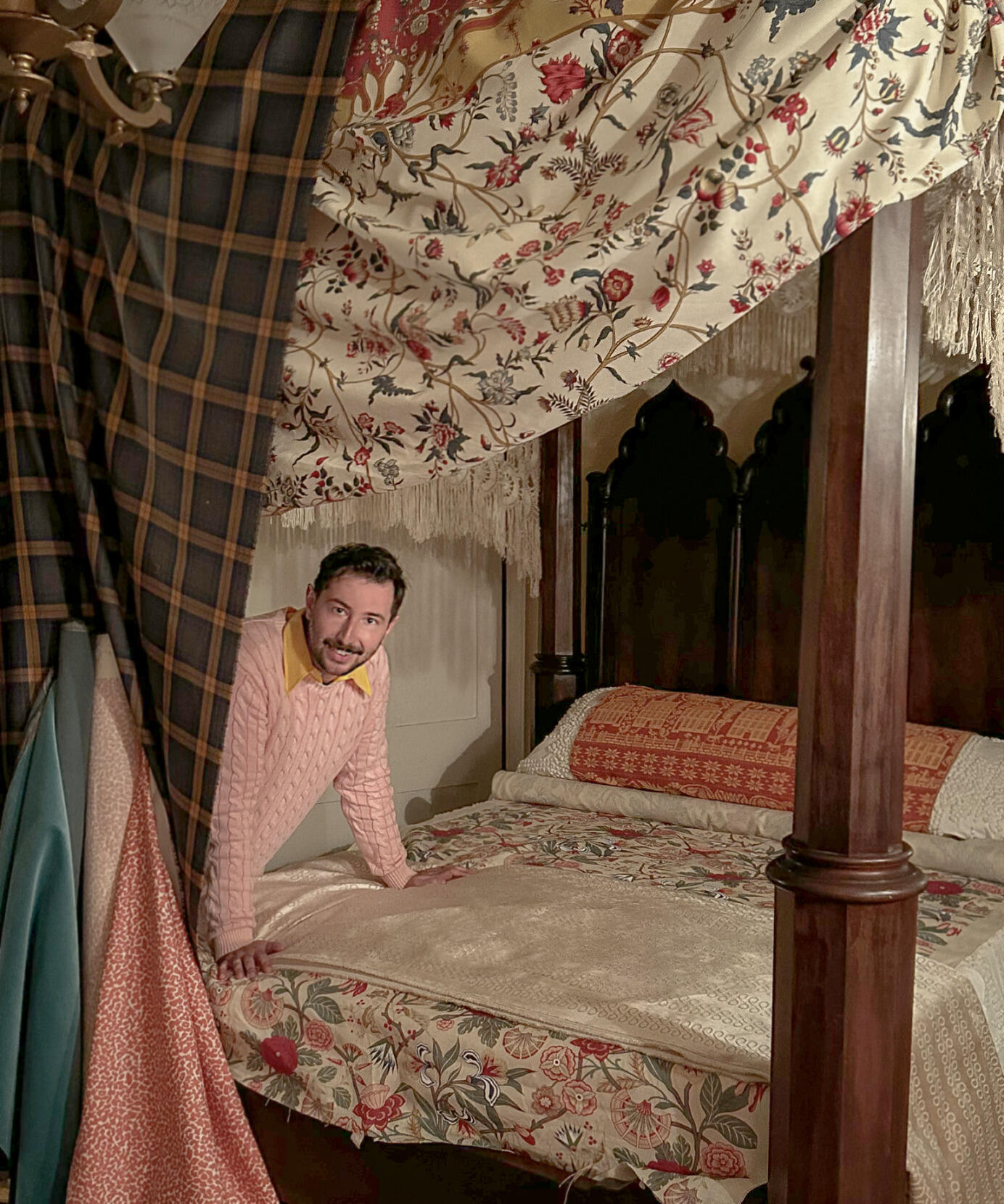 A photo of a man leaning onto the mattress of a canpoy bed
