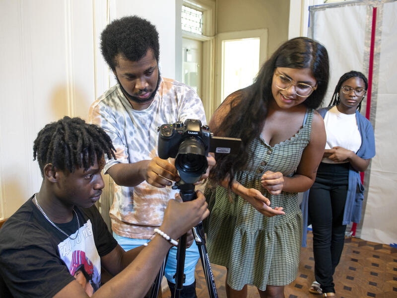 Three people looking at a camera and a woman behind them peeking over their shoulder 
