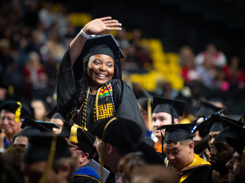 A student standing and waving during the commencement ceremony.