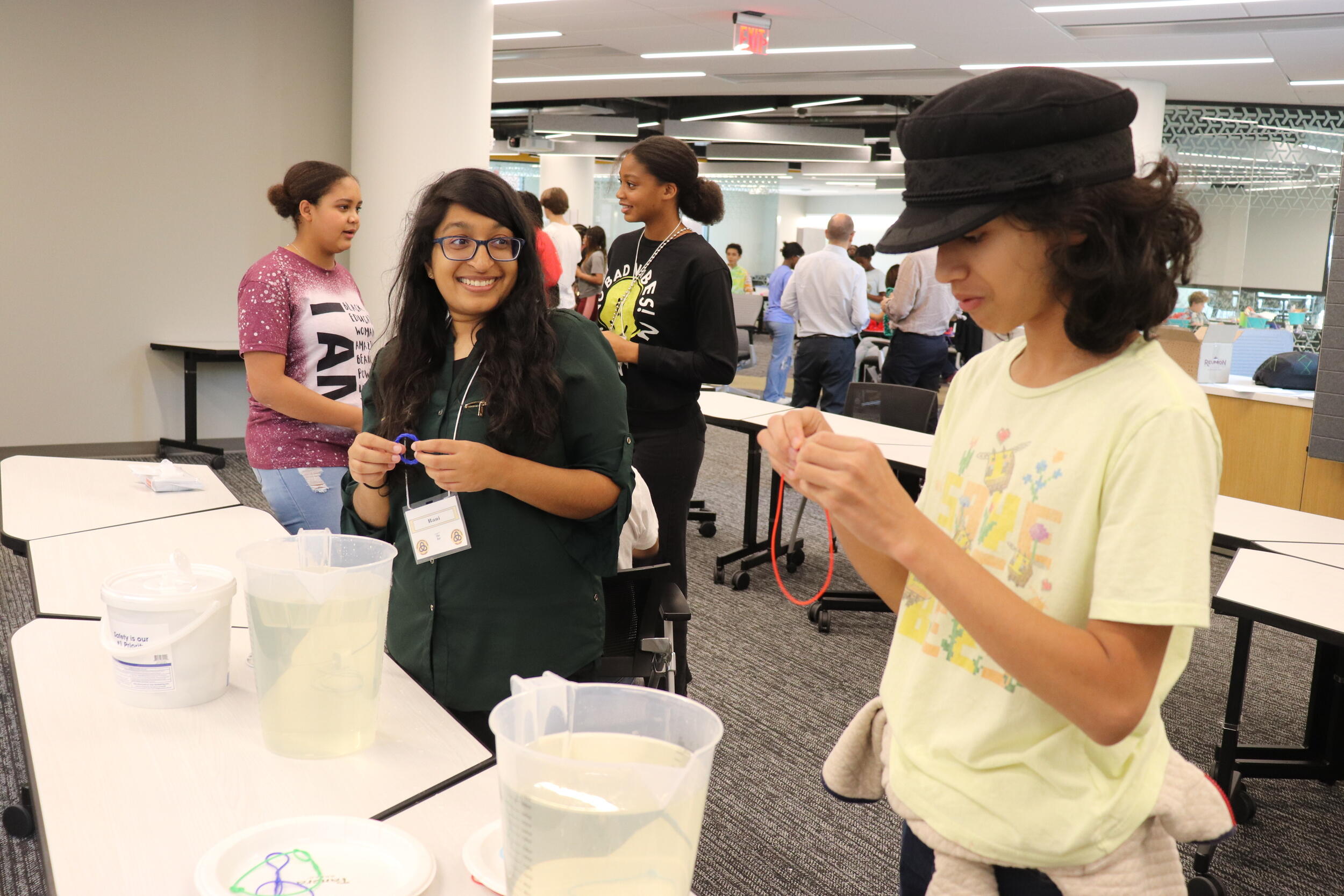 Two tenage girls holding pipes while standing in front of a table with jugs of water. 