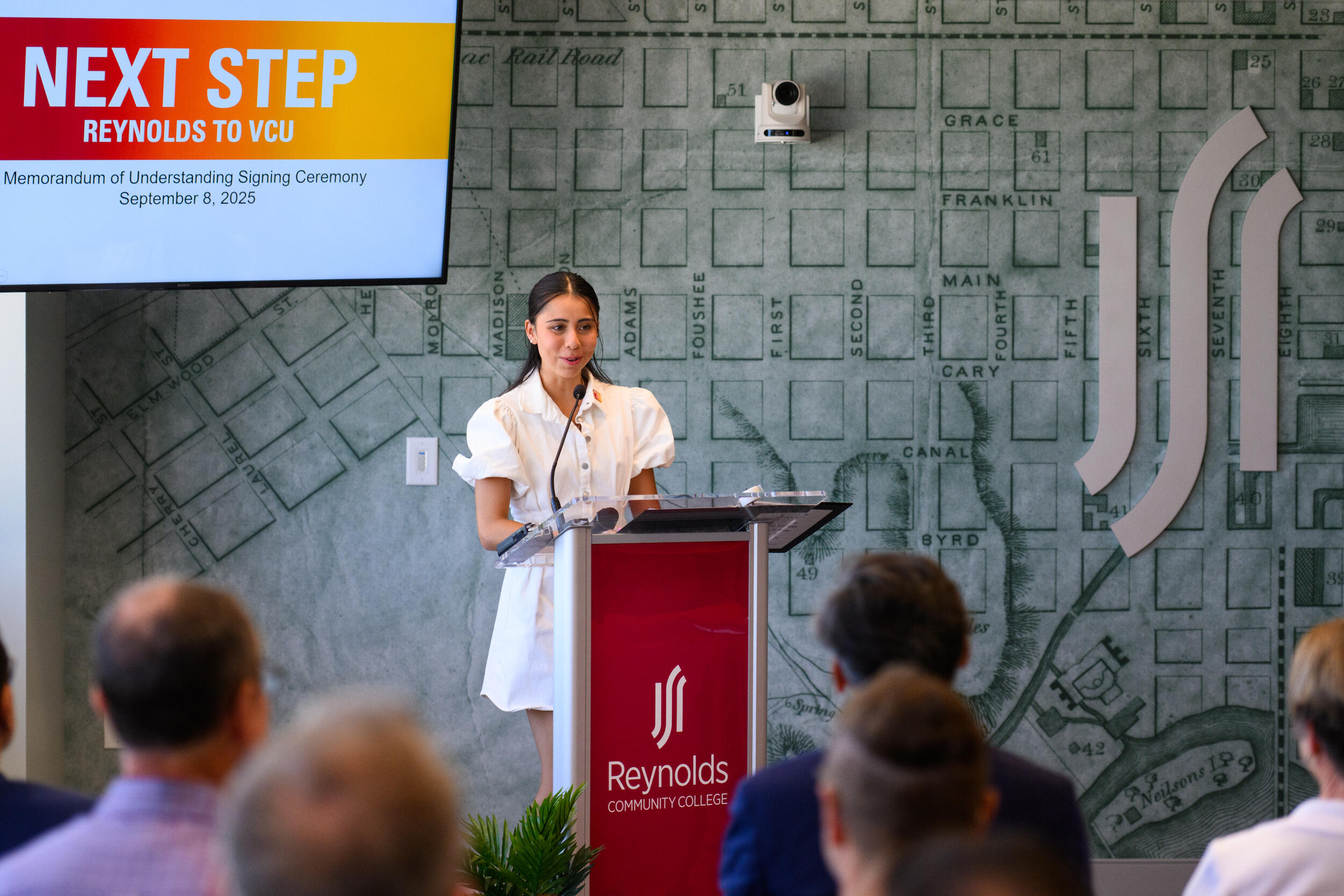 A woman speaking behind a podium to a crowd of people. 