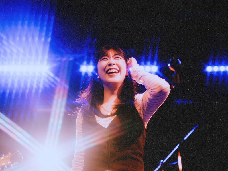 A smiling woman on stage with bright lights around her.