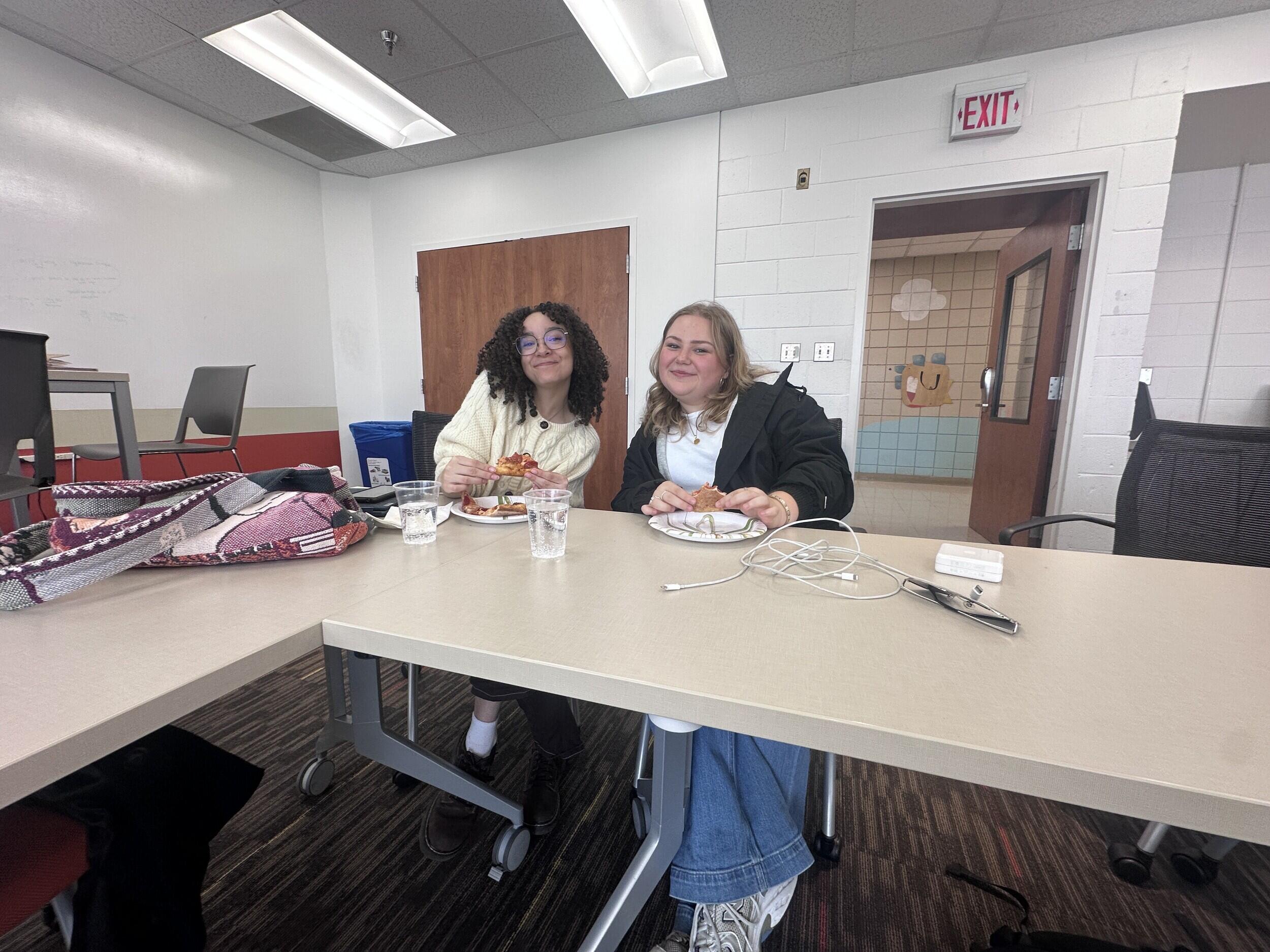 A photo of two women sitting at a table with paper plates in front of them