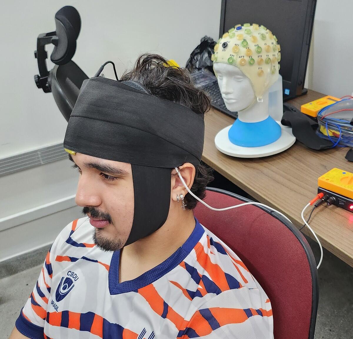 A photo of a man with a black headrap and a wire coming out of it. 