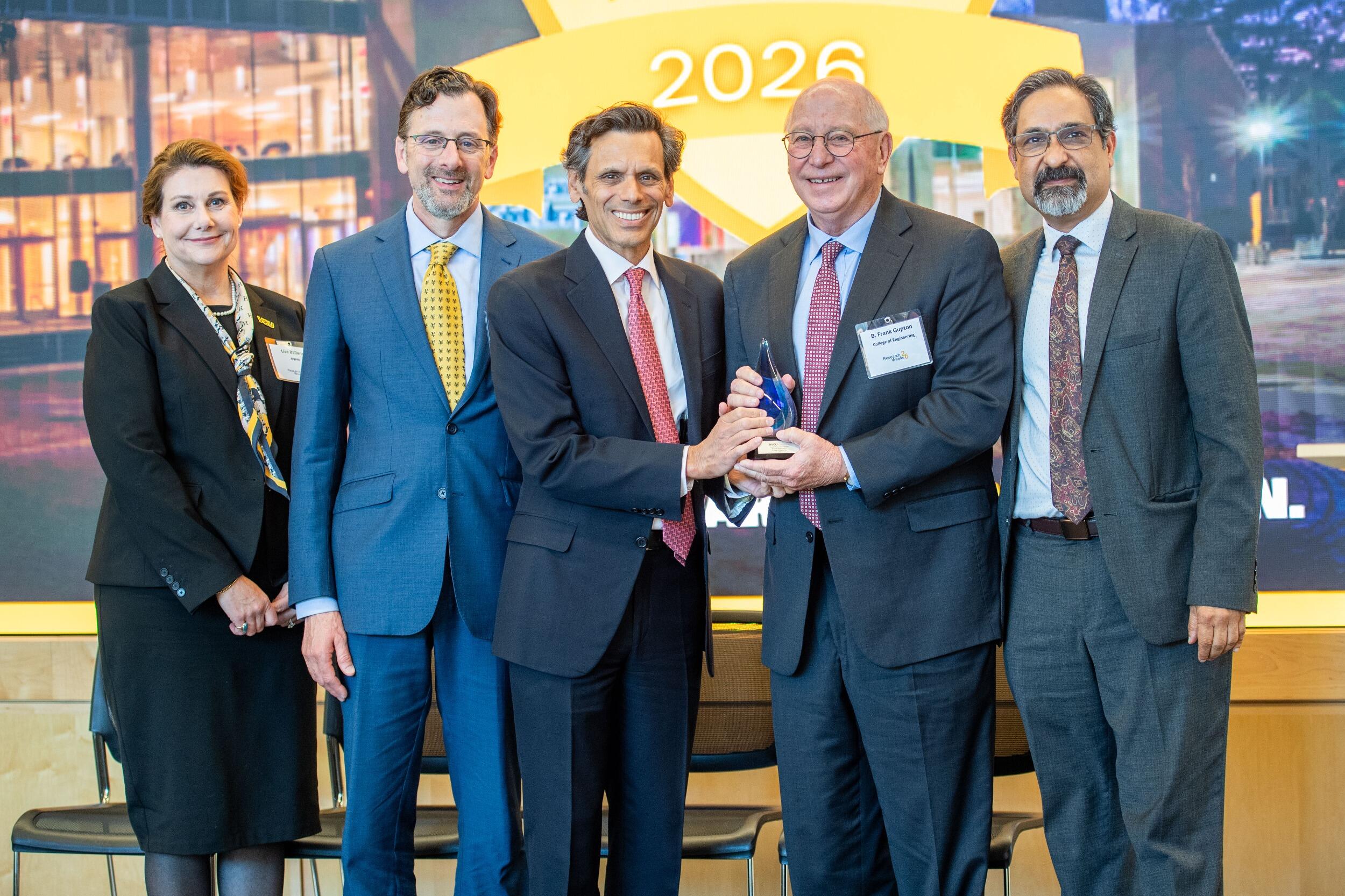 A group photo of four men and one woman standing. 