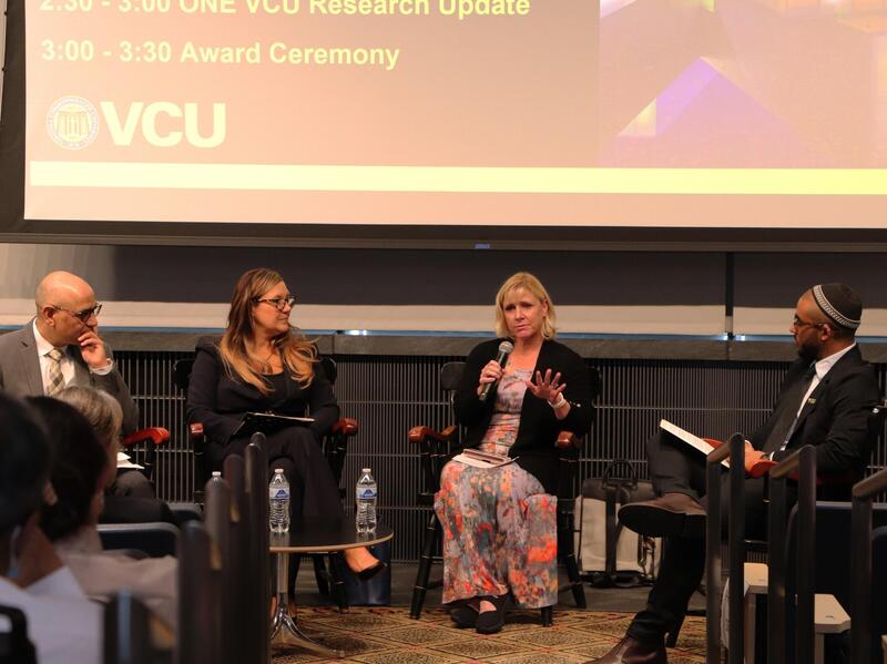 A photo of four people at the front of a room spekaing in front of a projector. 