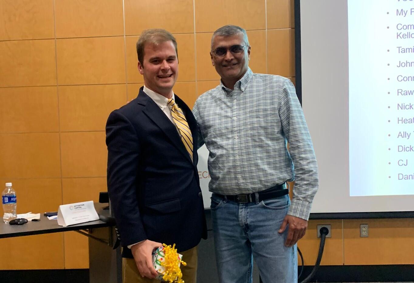 A photo of two men standing next to eachother. The both have one arm placed behind the other man's back. 