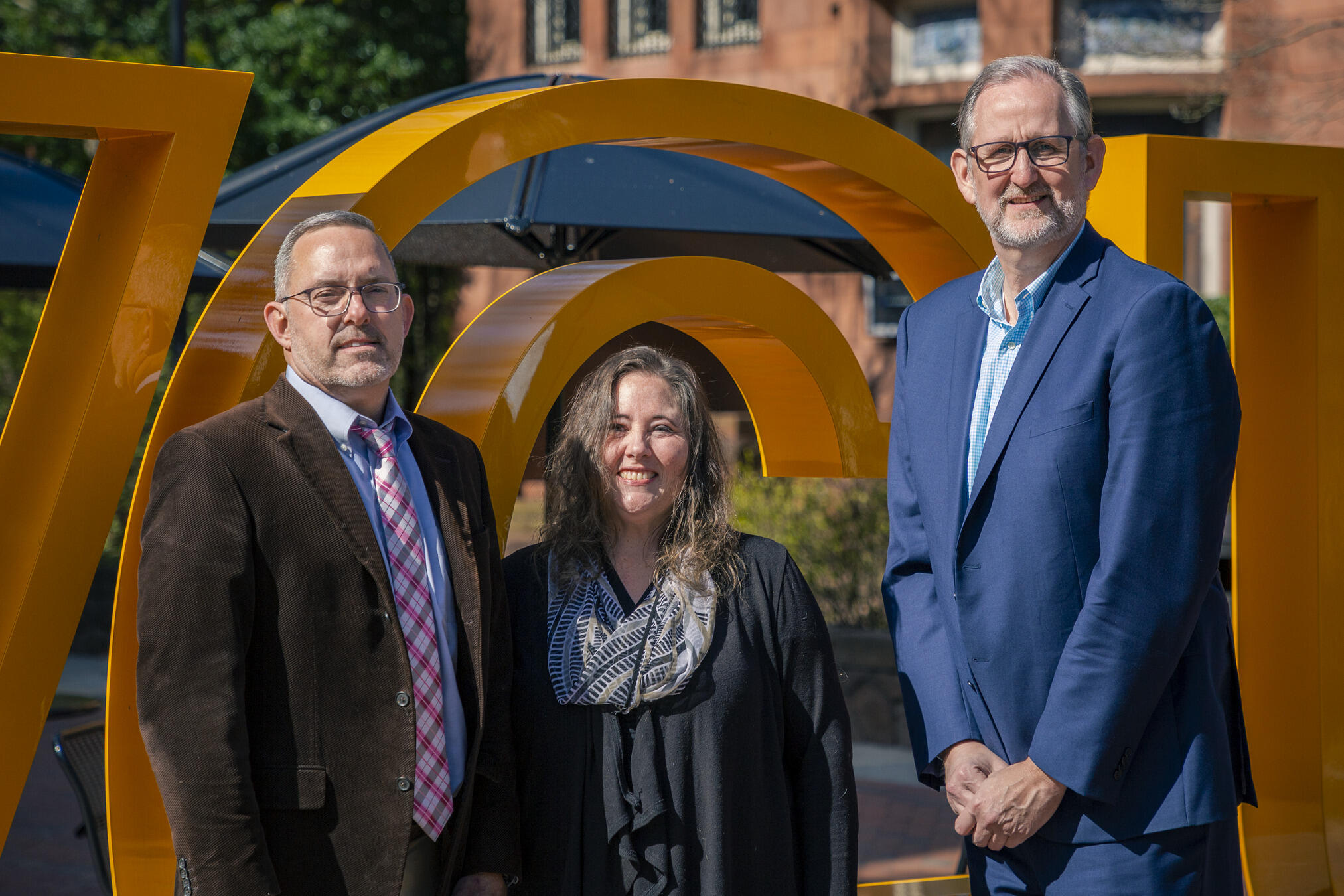 Three people standing in front of a giant letter \"C\"