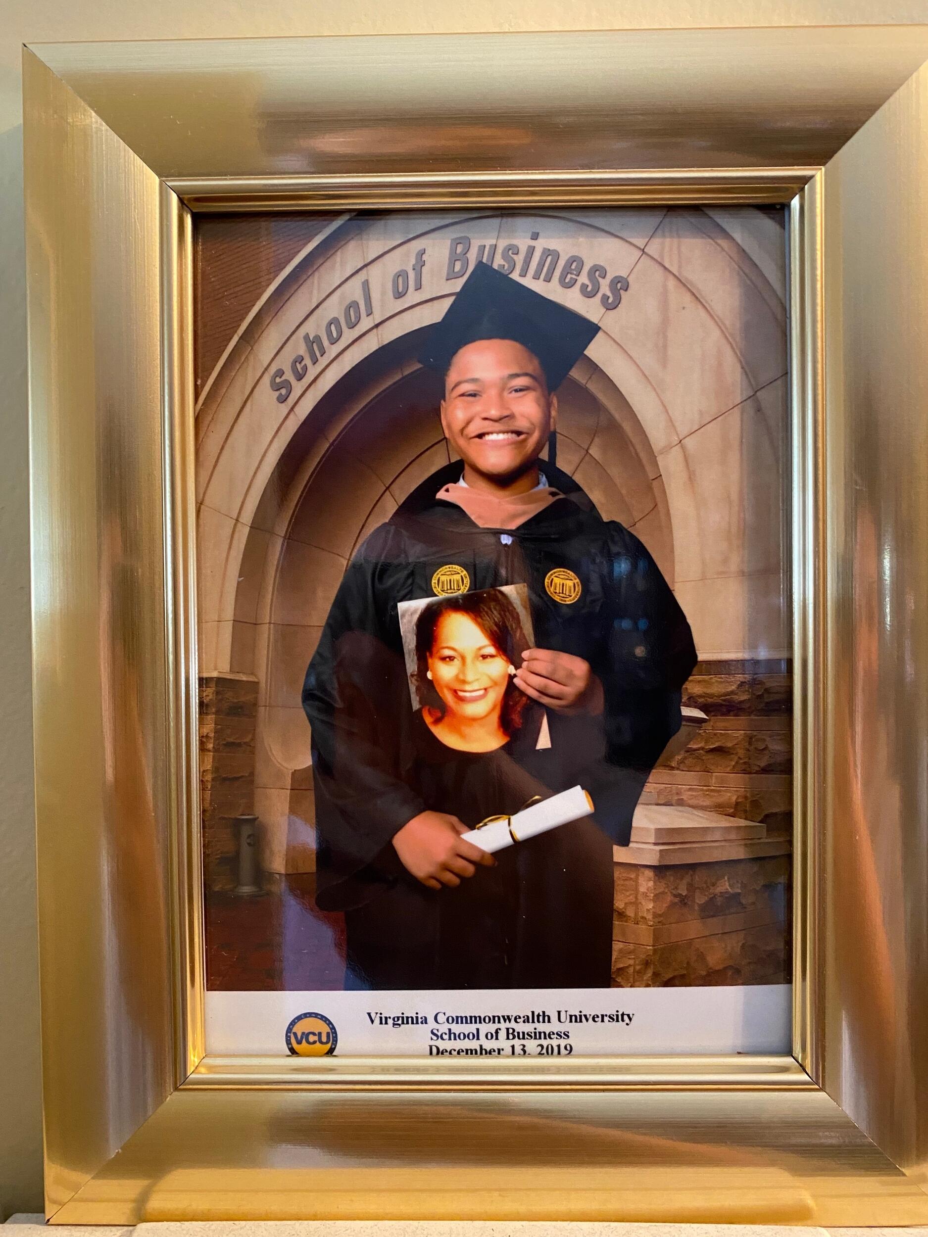 A photo in a frame that shows a man wearing a graduation cap and gown holding a diploma and holding a photo of a woman's face. 