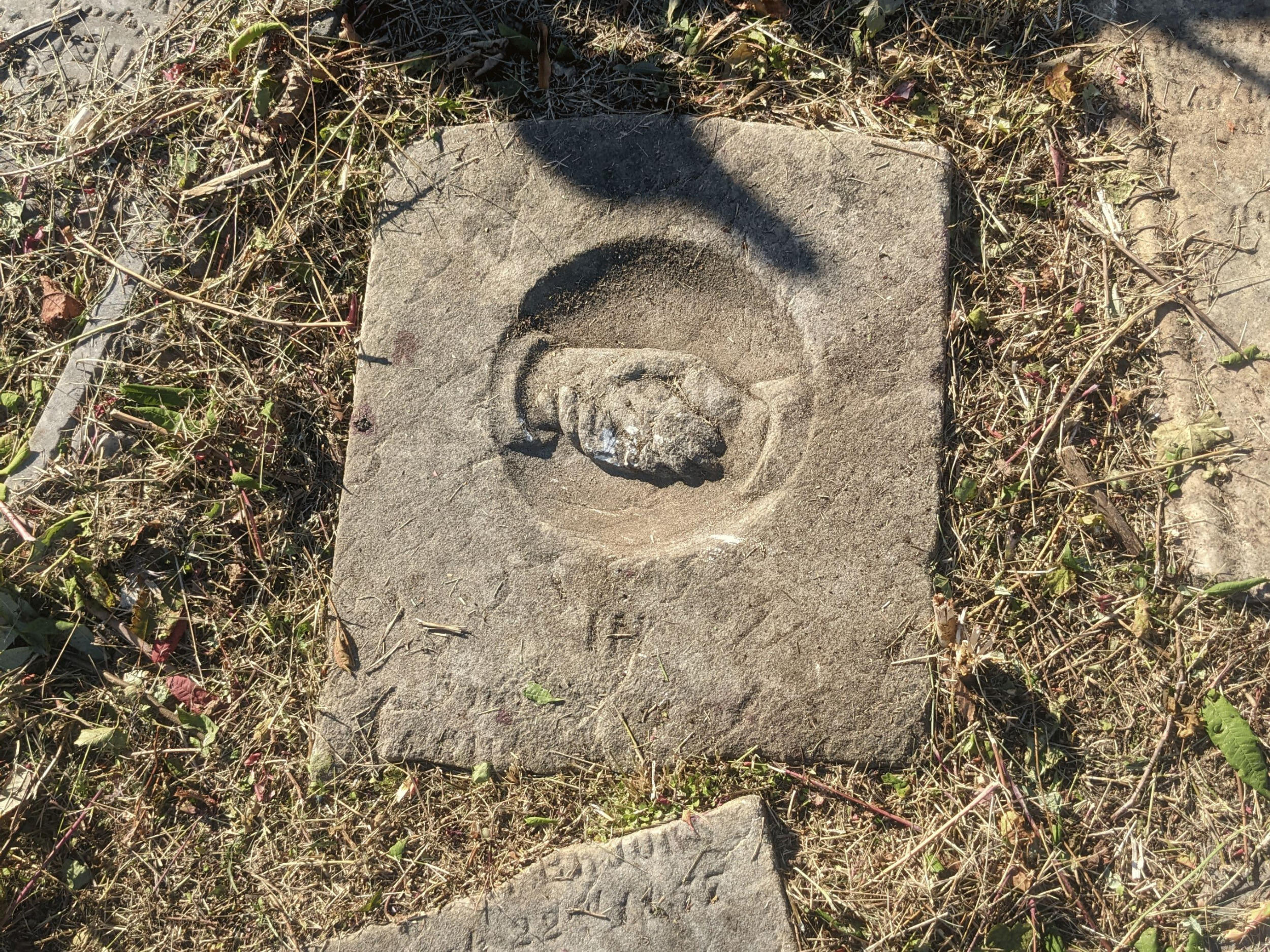 A stone on the ground with the chiseled image of hands clasped in a handshake.