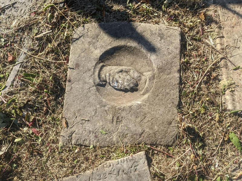 A stone on the ground with the chiseled image of hands clasped in a handshake.