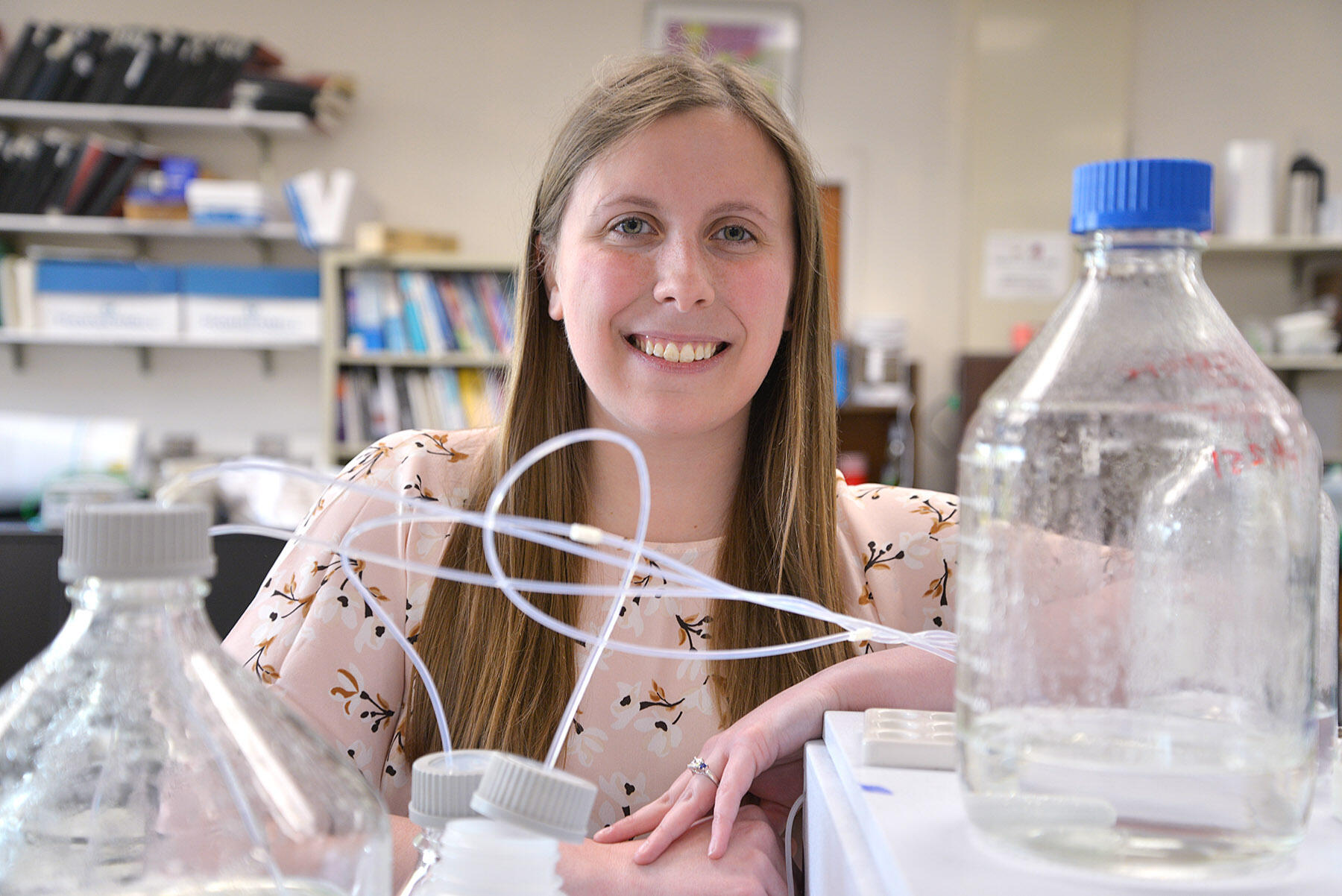 Woman behind table full of laboratory equipment.