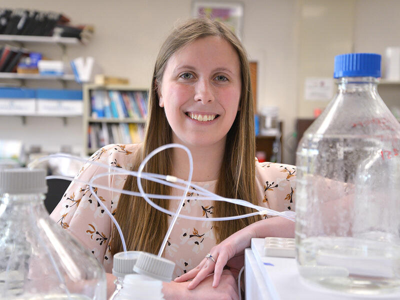 Woman behind table full of laboratory equipment.