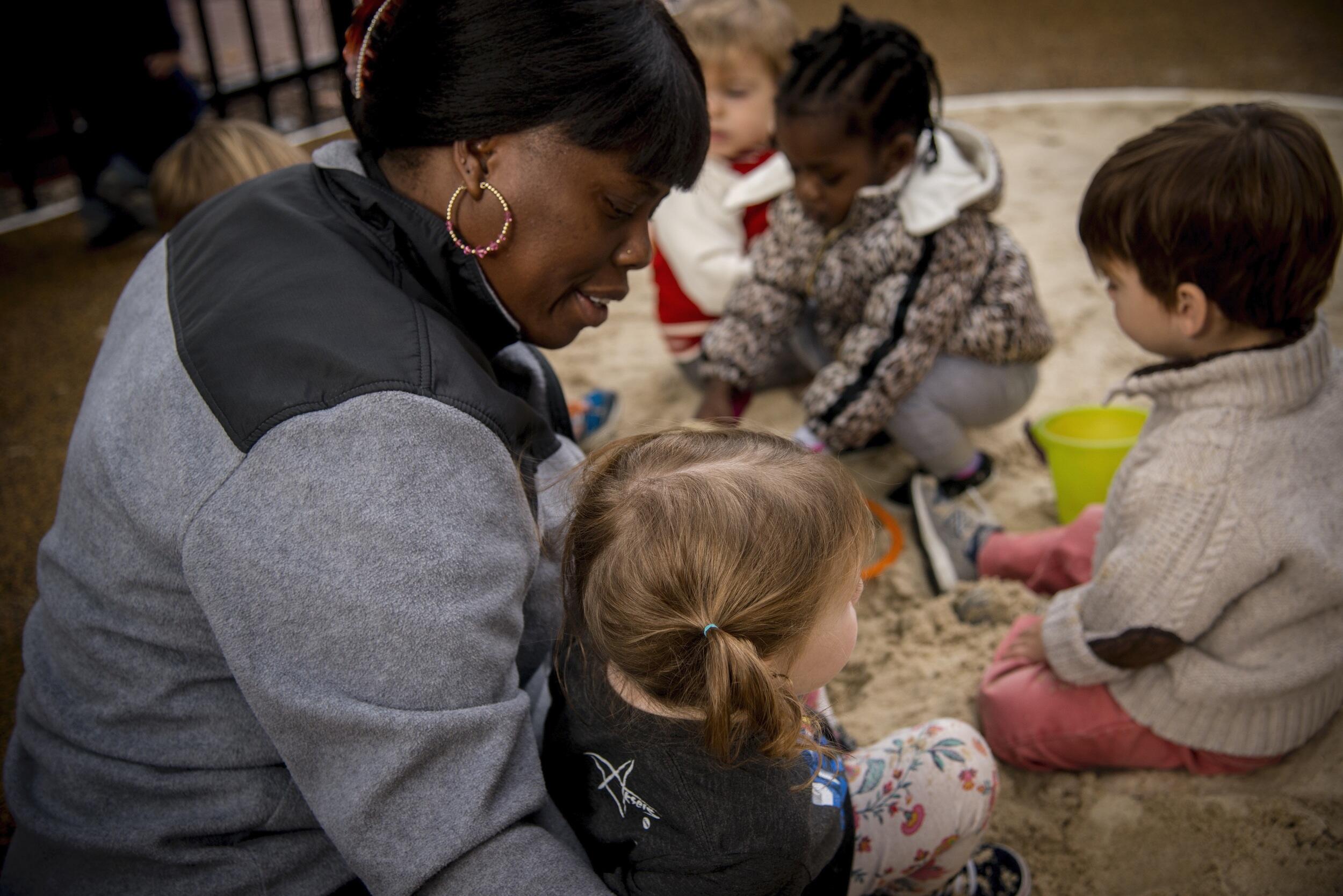 A teacher supervises children in a play area.