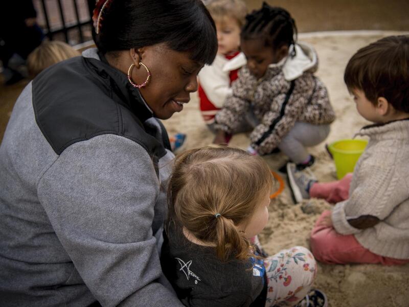 A teacher supervises children in a play area.