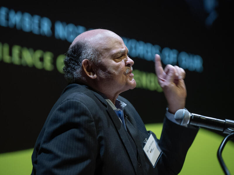 A photo of a man from the chest up speaking into a microphone. 
