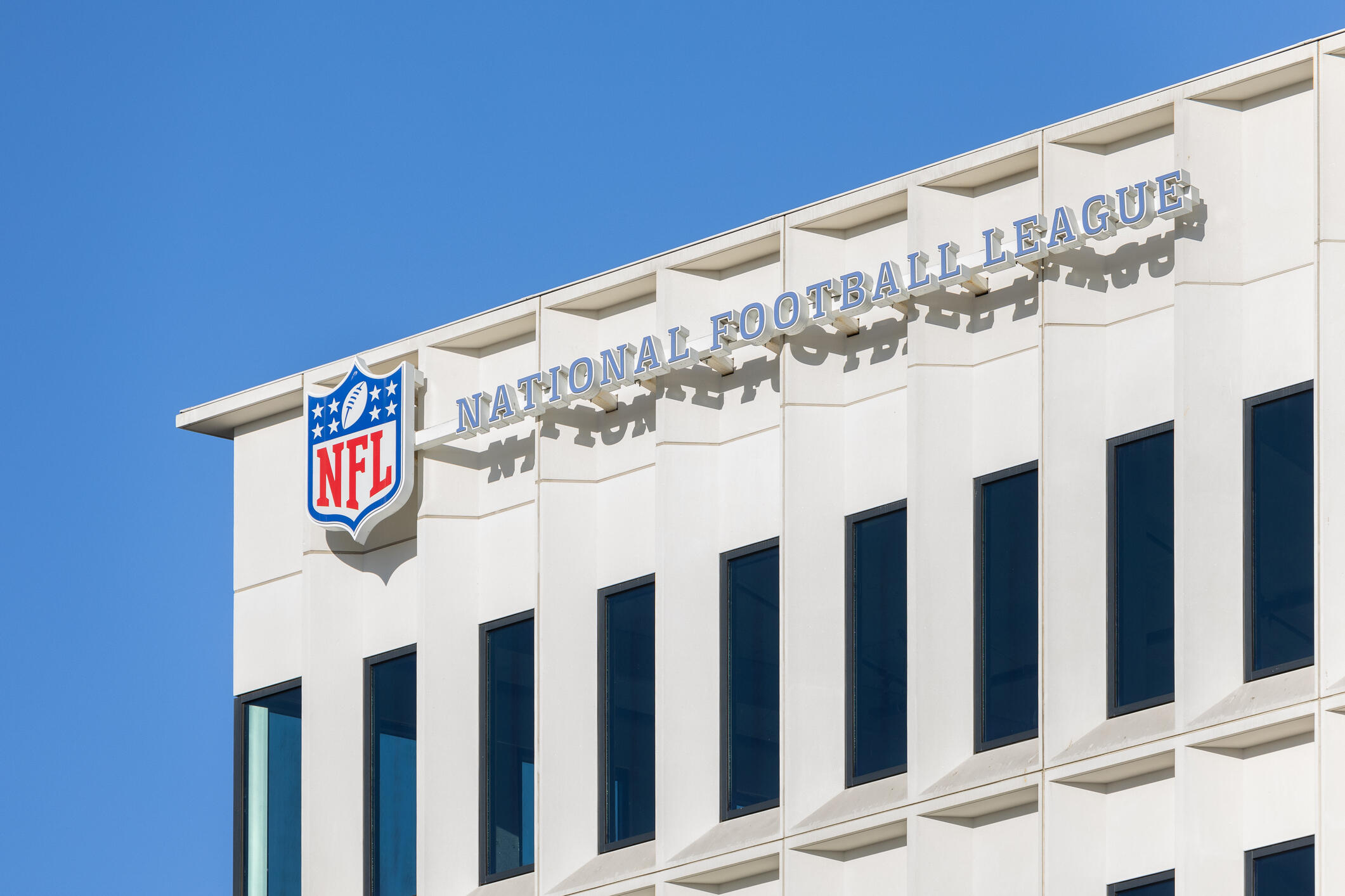A photo of an office building with a sign that says \"NATIONAL FOOTBALL LEAGUE\" in blue letters with a white outlet. 