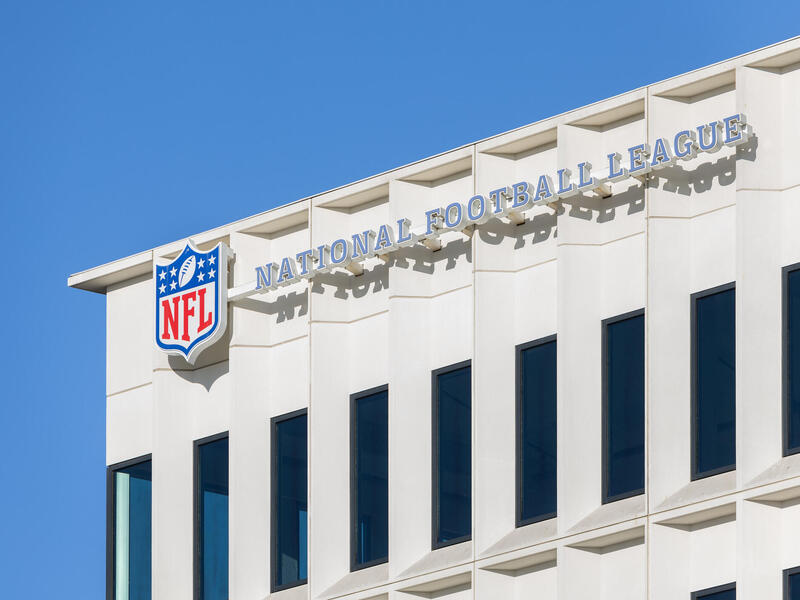 A photo of an office building with a sign that says \"NATIONAL FOOTBALL LEAGUE\" in blue letters with a white outlet. 