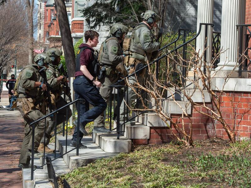 A photo of five people wearing police gear and guns walking up a flight of stairs.