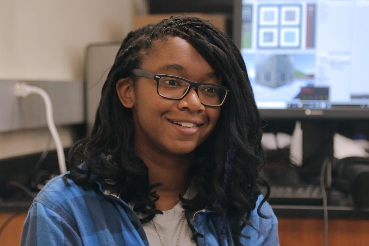 Woman seated, wearing glasses and jean jacket.