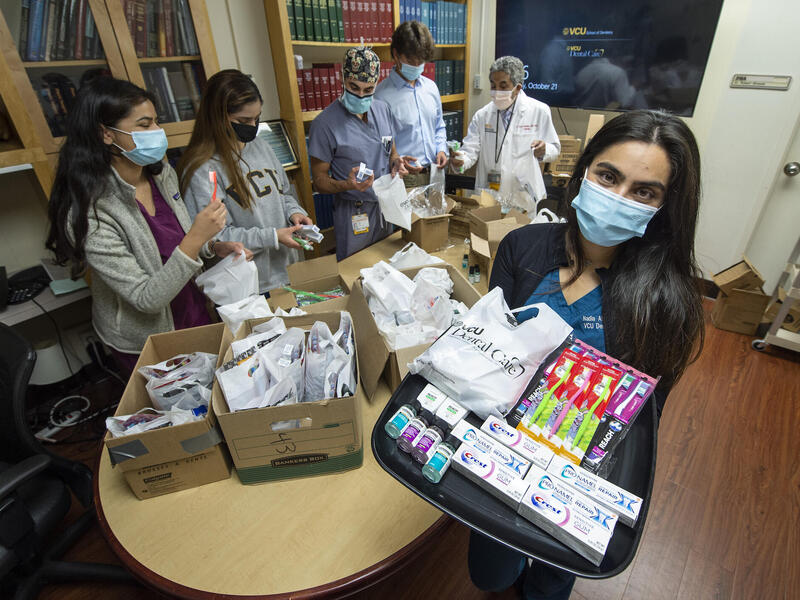Nadia Abdul-Ghafoor, far right, holding a dental supply kit in a conference room surrounded by classmates and faculty from the VCU dental school