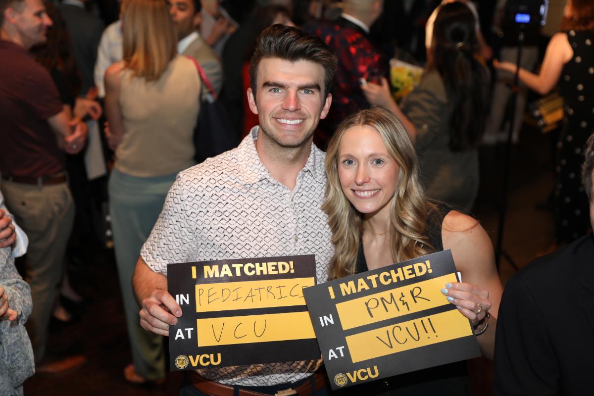 A photo of a a man and woman holding a black and yellow signs. The man is on the left and his sign says \"I MATCHED! IN PEDIATRICS AT VCU\" At the bottom of the sign is the VCU logo. The woman is on the right and his sign says \"I MATCHED! IN PM & R AT VCU\" At the bottom of the sign is the VCU logo. 