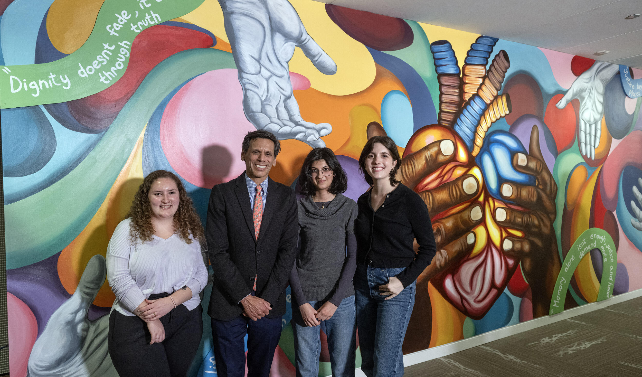 A photo of four people standing in front of a colorful wall mural. 