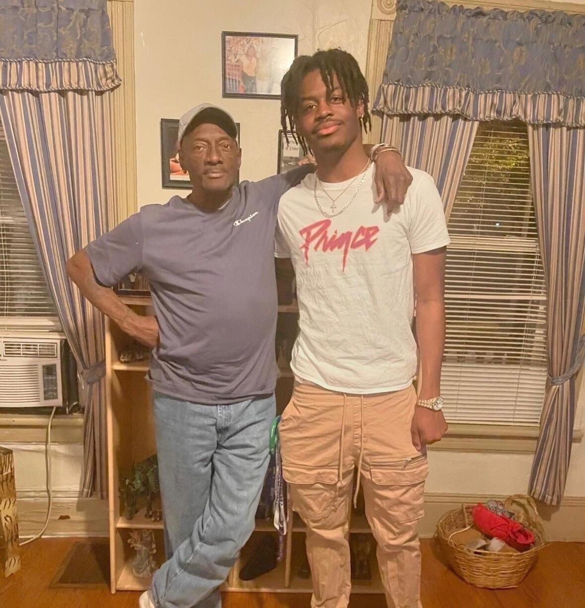 A photo of two men standing next to each other. The man on the left has his arm around the man on the right's shoulder. 