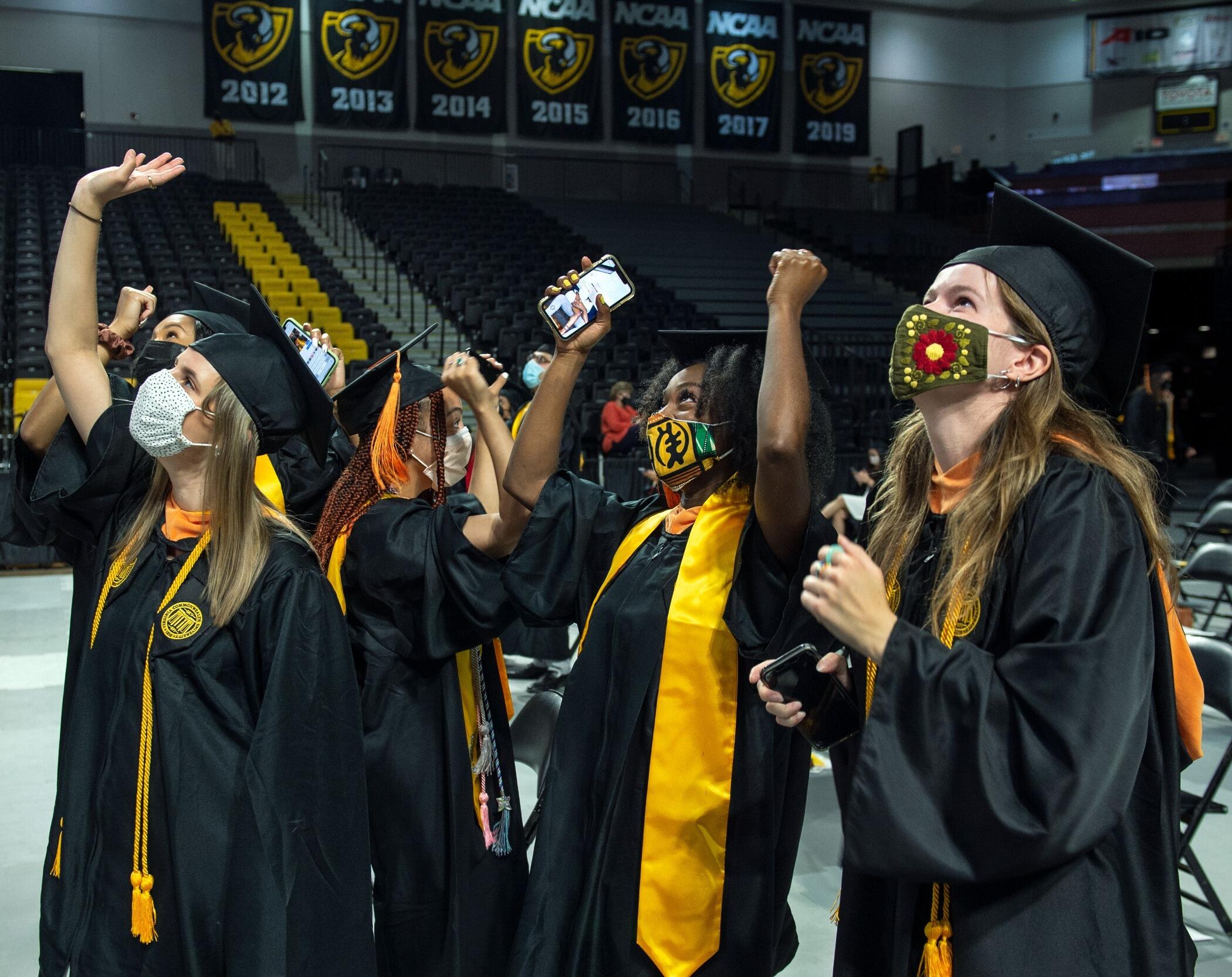 Graduates in caps and gown raise their arms in celebration.