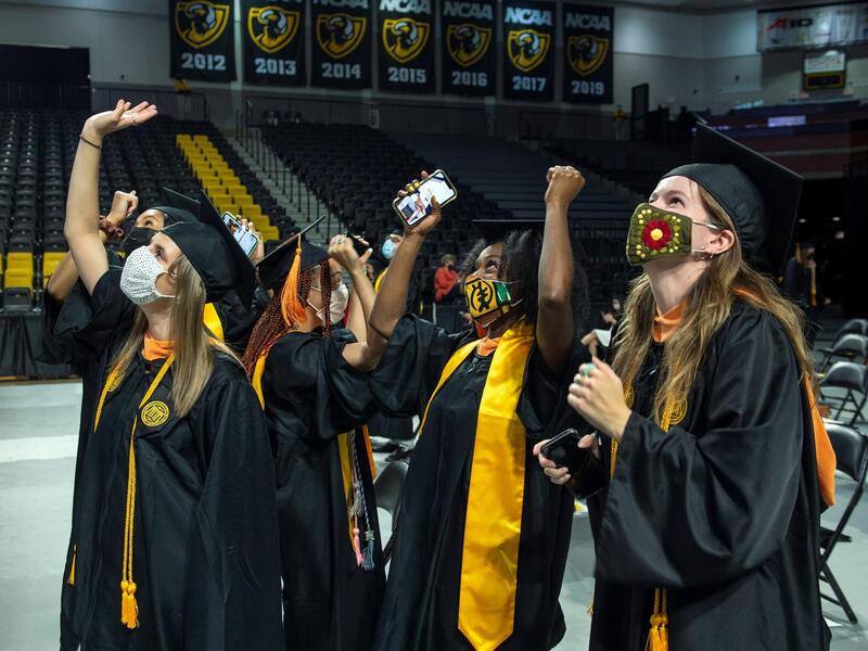 Graduates in caps and gown raise their arms in celebration.