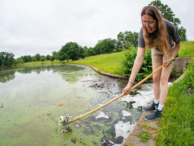 A photo of a woman scooping water out of a lake. 