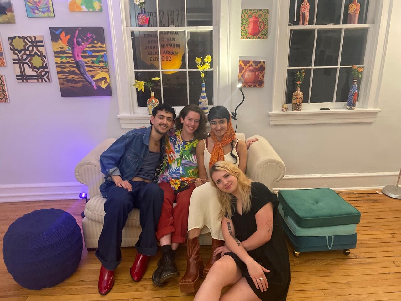 Three people sitting on a couch and one person sitting on the floor in front of them. 