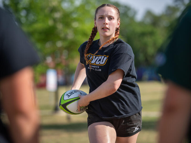 A photo of a woman holding a ball and running on a field.