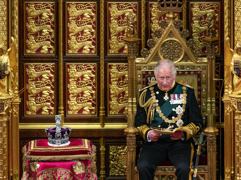 King Charles III sits on a throne with a crown resting nearby.