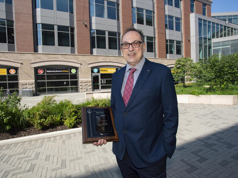 A man standing in front of a building holding an award plaque. 
