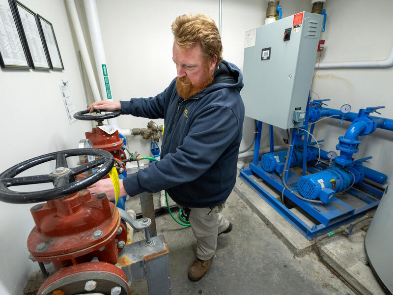 A man in a blue jacket checks back flow and booster pumps.