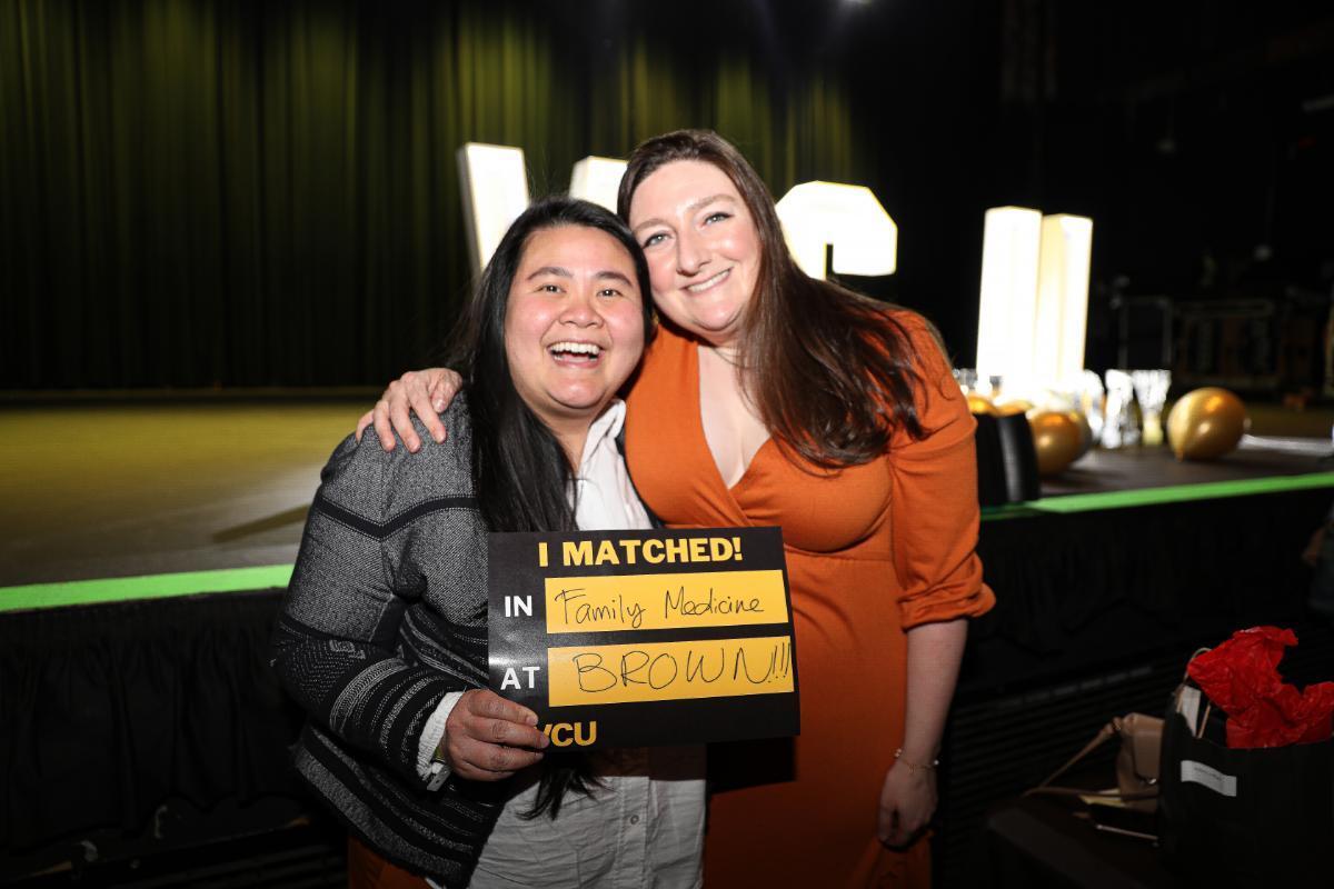 A photo of a two women, with the woman on the left holding a black and yellow sign that reads \"I MATCHED! IN Family medicine AT BROWN!!!.\" At the bottom of the sign is the VCU logo. 