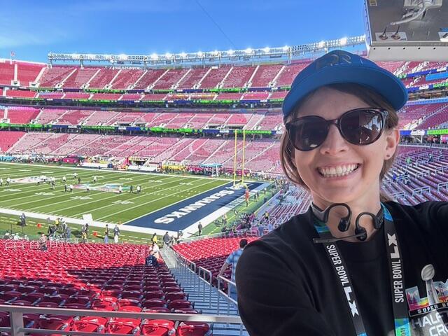 A photo of a woman standing in the bleachers of a large football stadium. 