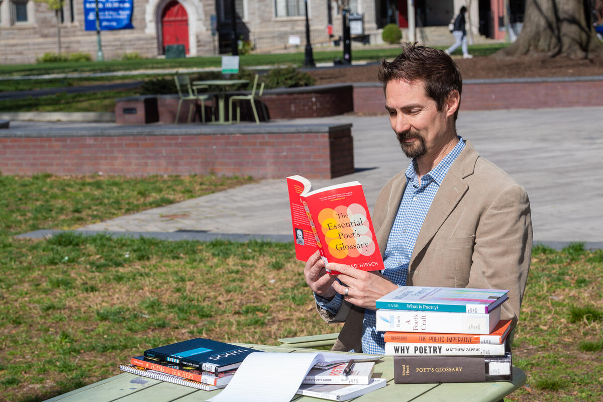 A man reading from a book with a stack of books next to him