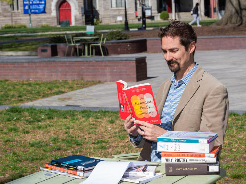 A man reading from a book with a stack of books next to him