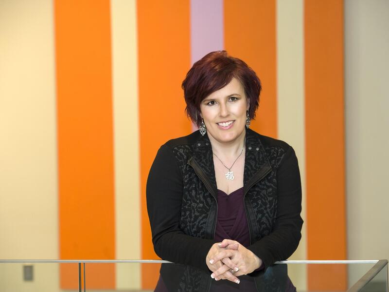 A photo of a woman smiling and learning on a glass railing. 