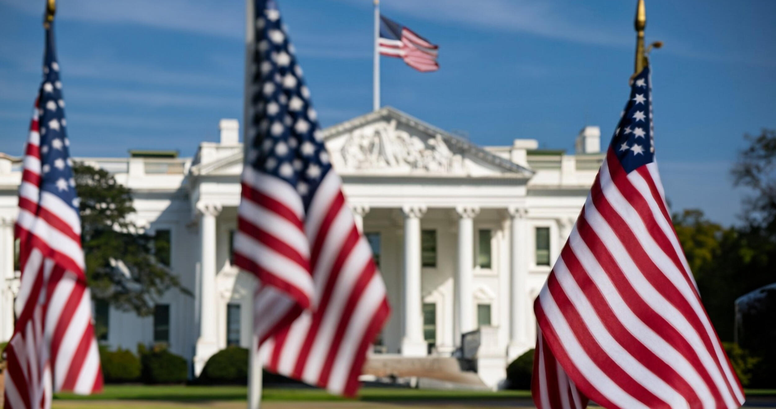 A photo of three American flags in front of the White House. 