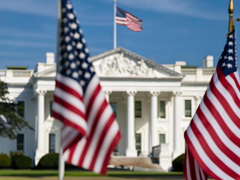 A photo of three American flags in front of the White House. 