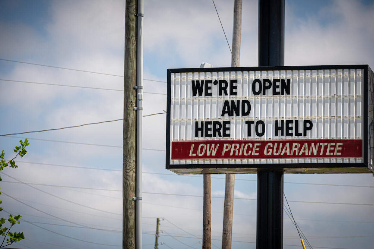 A sign for a business stating \"We're open and here to help. Low price guarantee.\"