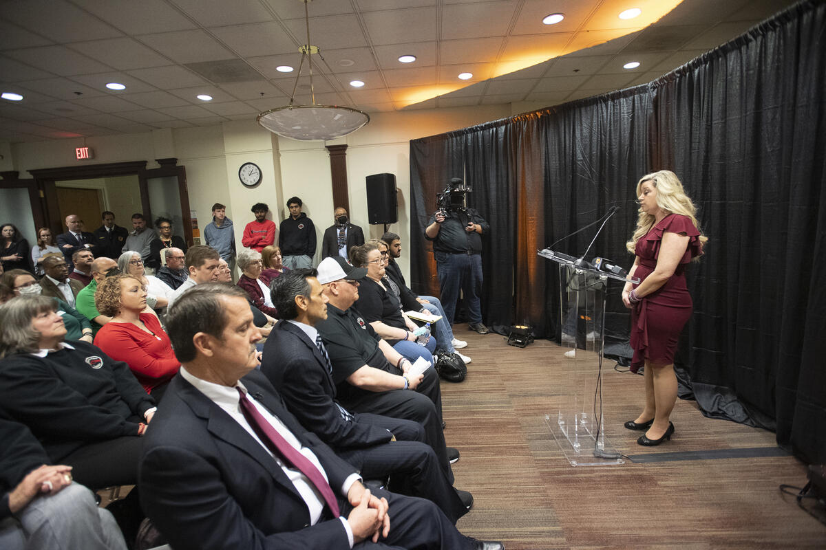 A woman speaking at a podium in front of a room full of people. 