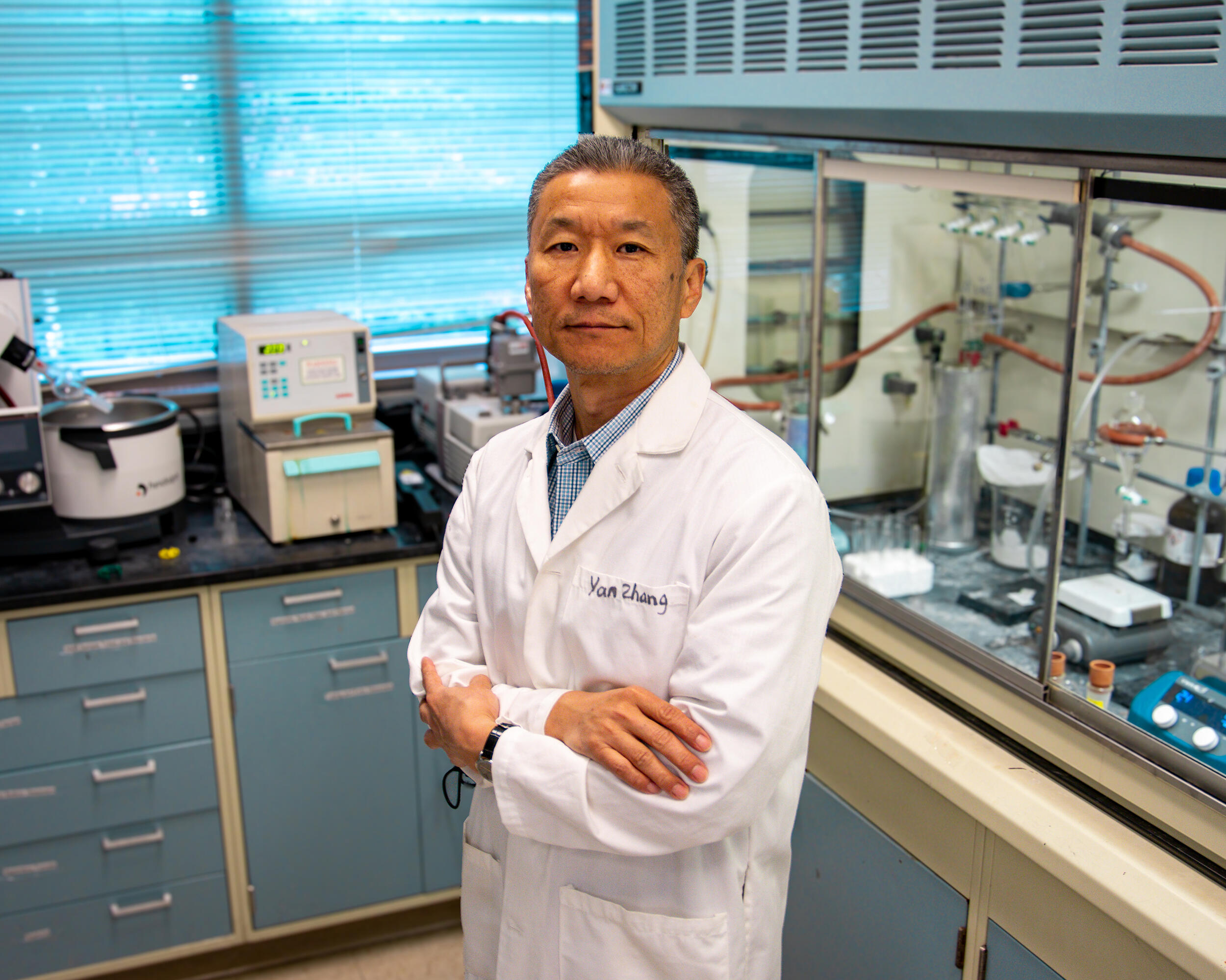 A photo of a man in a white lab coat standing in the middle of a research lab. 