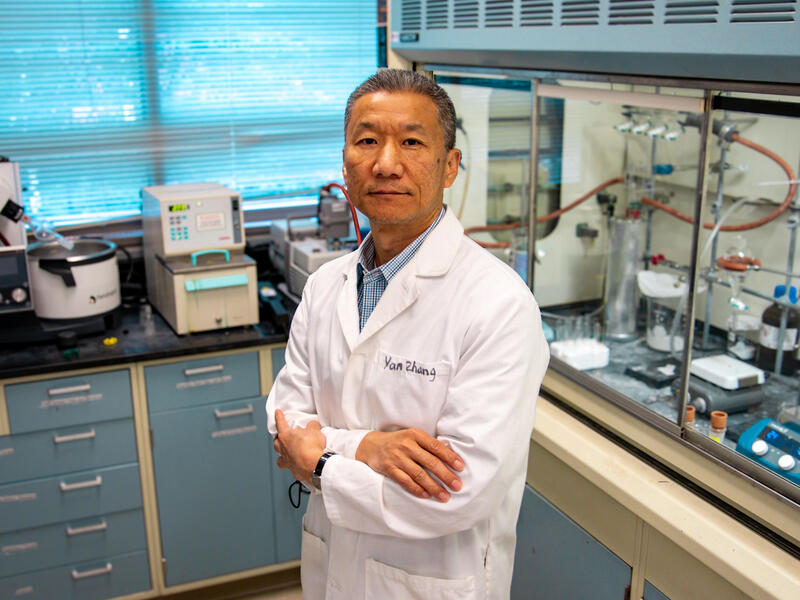 A photo of a man in a white lab coat standing in the middle of a research lab. 