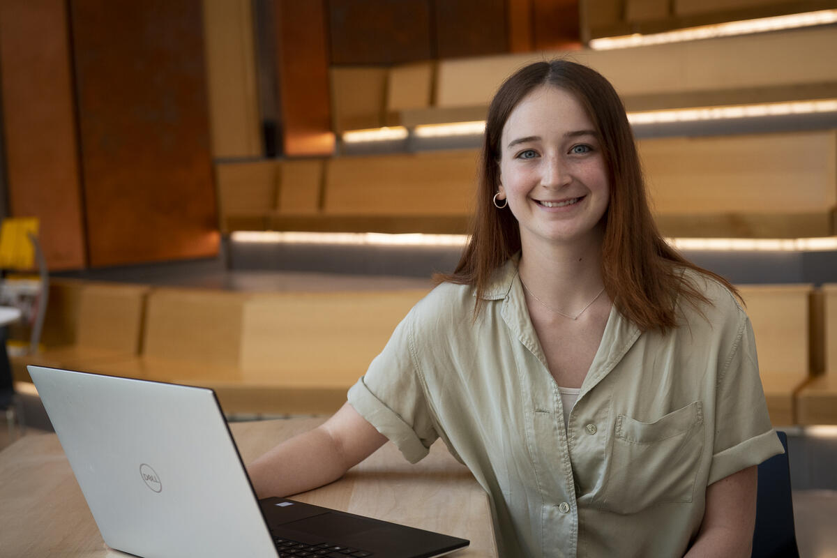 A woman sitting in a lecture room with a laptop in front of her 
